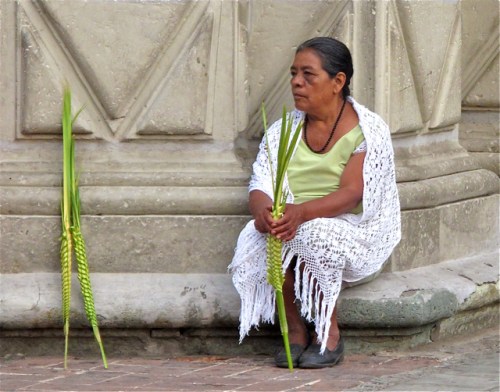 Woman seated on stoop with palm fronds.