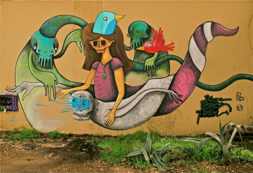 Colorful street art on wall with female skeleton, bird, and serpent
