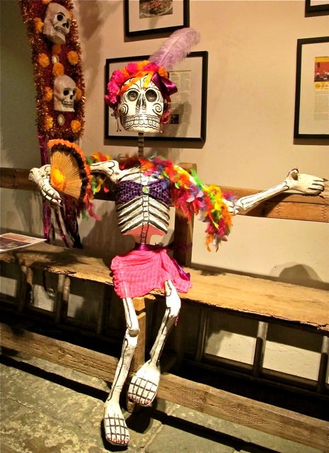Skeleton in pink skirt and feather boa seated on a bench
