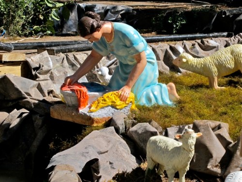 Female mannequin washing clothes as mannequins of lambs watch.