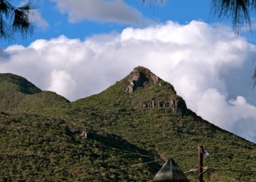Green rocky top mountain against white cloud and blue sky
