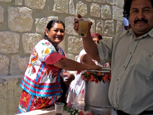 Woman in indigenous dress serving an agua, man in foreground holding cup