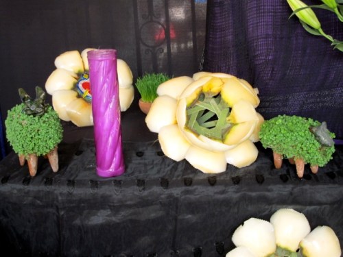 Close up of 2 "chia pets," candle, and palm flowers.