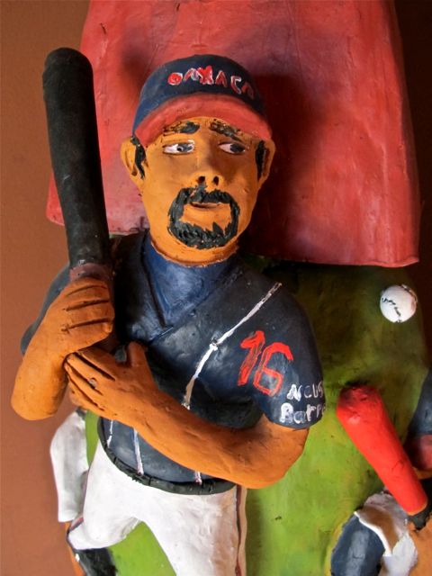 Closeup of baseball player on sculpture with bat on shoulder, wearing Guerreros de Oaxaca cap and jersey.