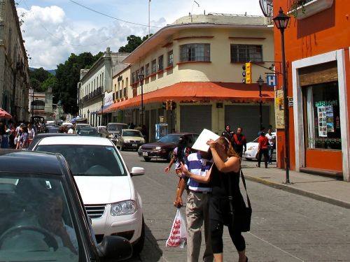 Street scene (in color) filled with automobiles and people on sidewalk and a couple crossing the street