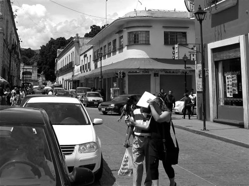Black and whte street scene filled with automobiles and people on sidewalk and a couple crossing the street