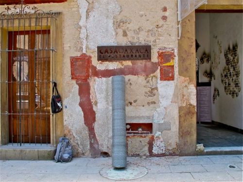 Roll of chicken wire leaning up against chipped wall of under Casa Oaxaca sign