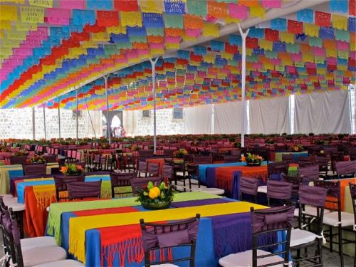 Interior of large tent decorated with multicolor tableclothes and papel picado on ceiling