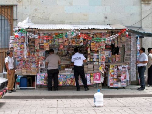 People standing in front of newsstand decorated with a green, white, and red garland.
