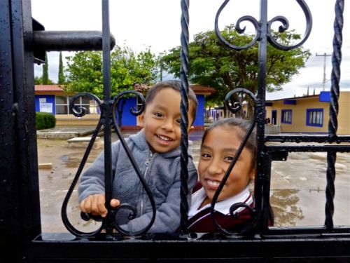 Smiling girl holding smiling small boy behind decorative iron bars