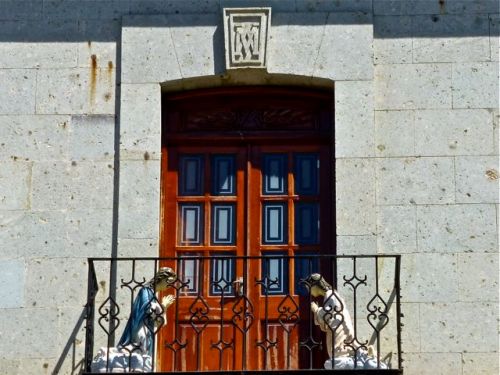 Two kneeling statues of Mary behind balcony railing on either side of a door