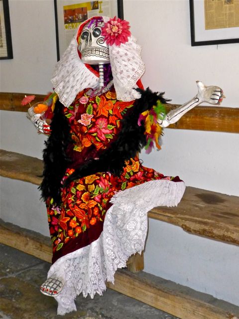 Seated Catrina in Tehuana traje holding cocktail glass with umbrellas.