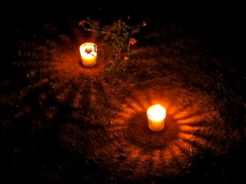 Night shot of two lighted votive candles casting halos on the ground