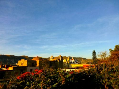 Blue sky, African tulip trees in foreground, churches in mid-ground, mountains in distance.