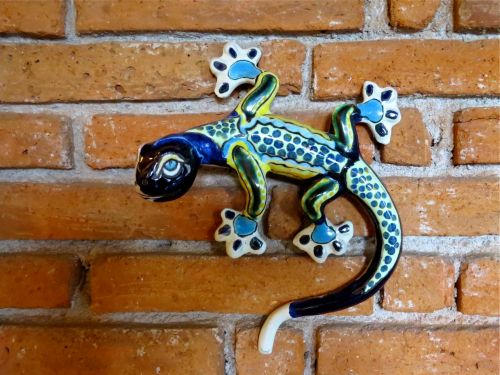 Blue, green, yellow and white ceramic gecko on brick wall.