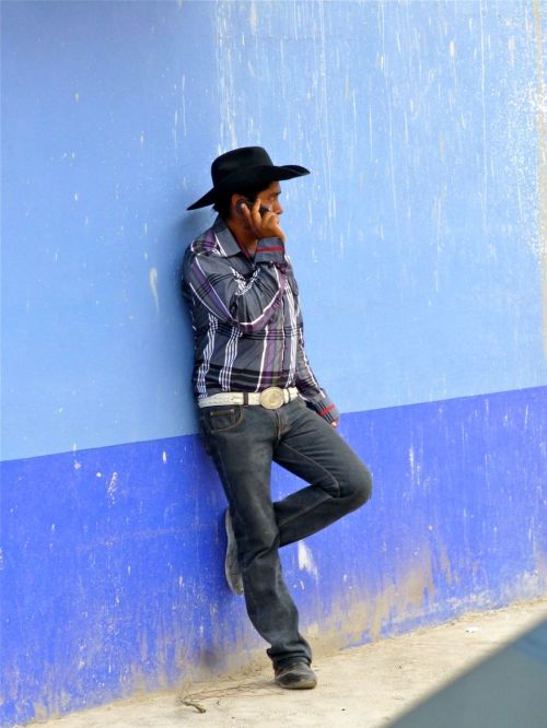 Young man leaning against blue wall talking on cell phone